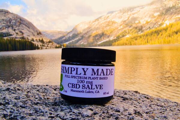 A jar of cbd salve sitting on the side of a lake.